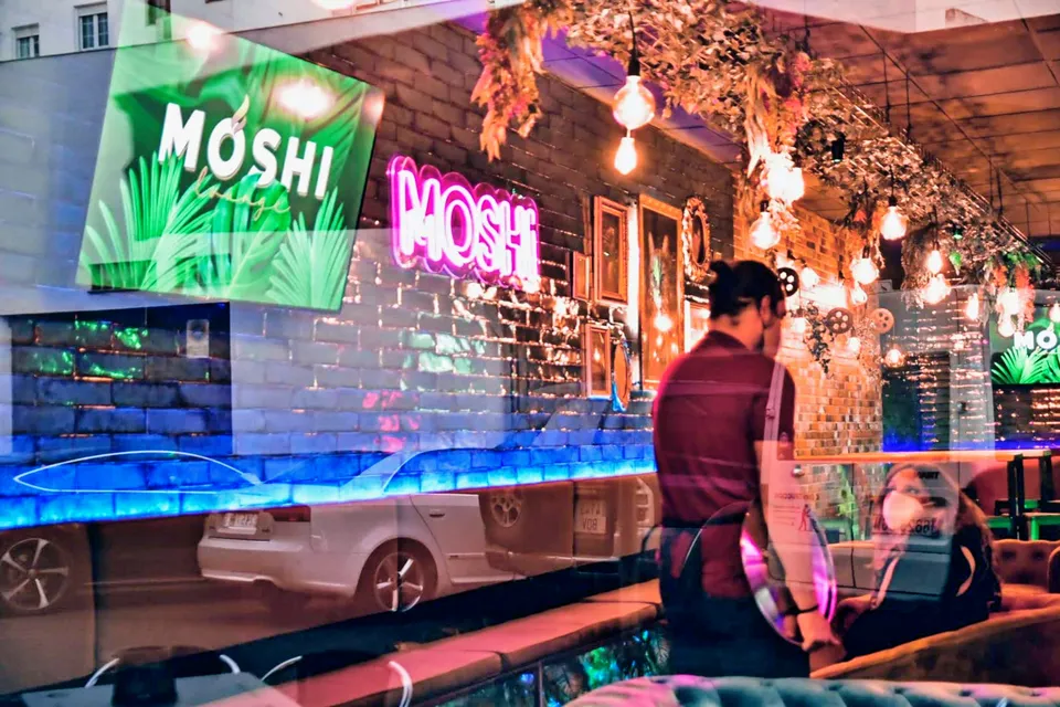 Interior de Moshi Lounge con vegetación, luces cálidas y sofás Chester